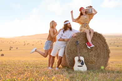 Happy hippie friends with radio receiver and guitar in field, space for text