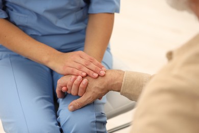 Photo of Nurse supporting elderly patient indoors, closeup view