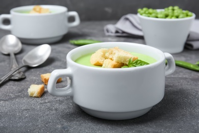 Photo of Green pea soup with croutons in bowl on table