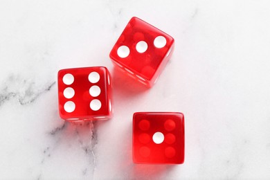 Photo of Three red game dices on white marble table, flat lay