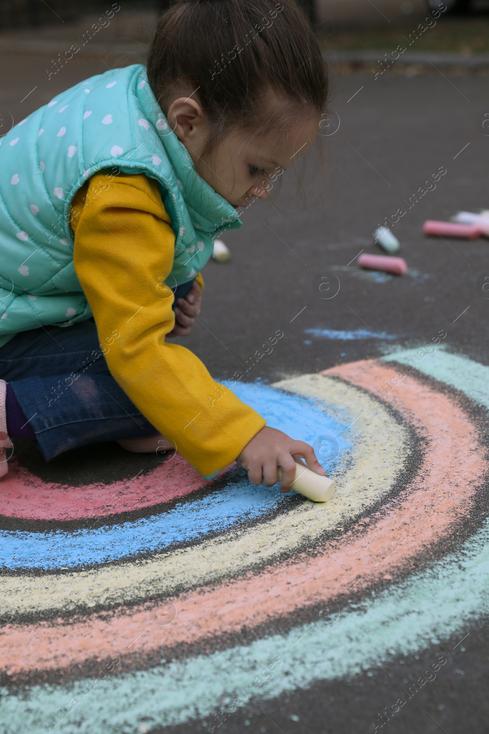 Photo of Child drawing rainbow with chalk on asphalt