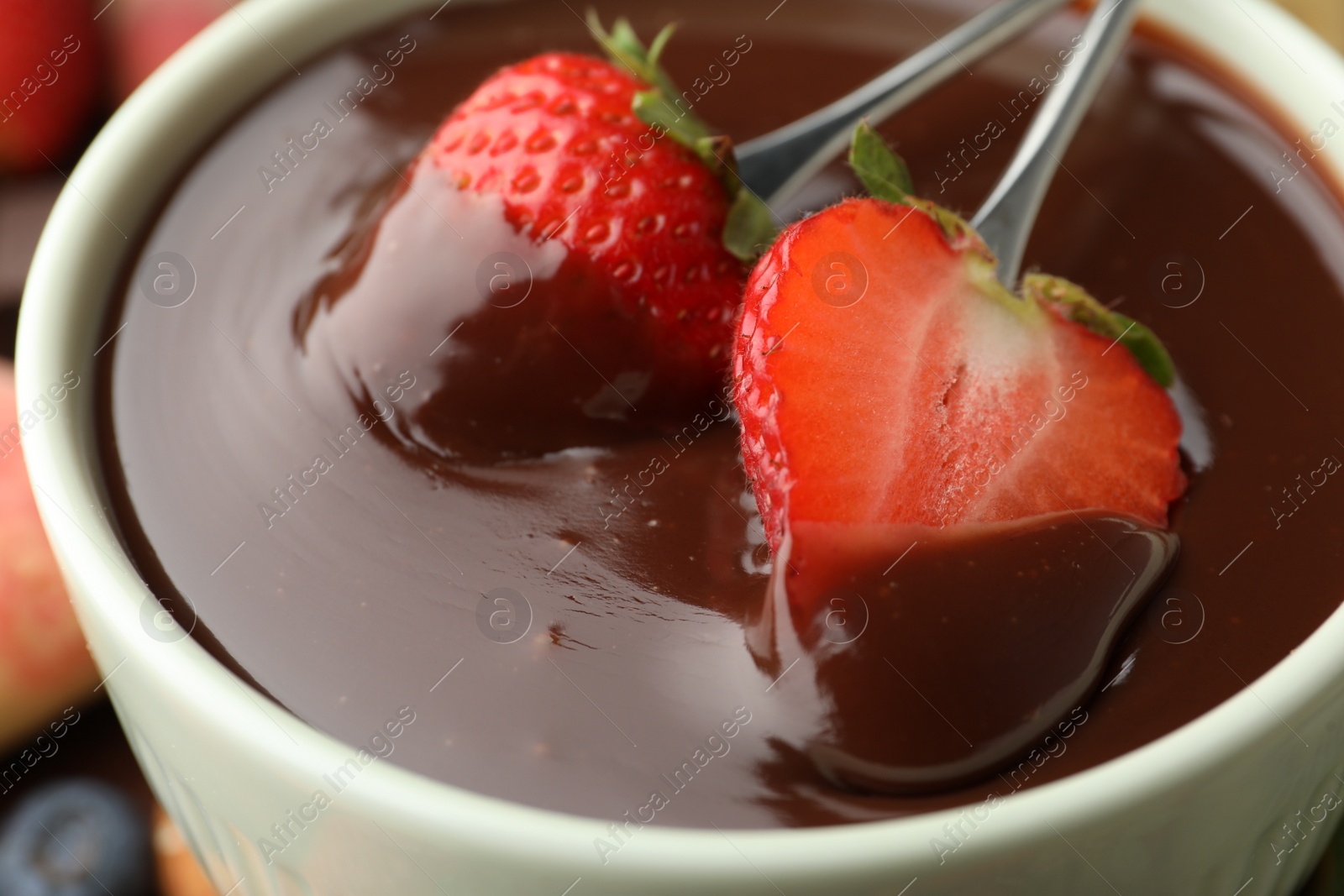Photo of Fondue forks with strawberries in bowl of melted chocolate, closeup