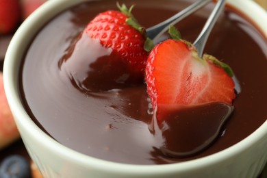 Photo of Fondue forks with strawberries in bowl of melted chocolate, closeup