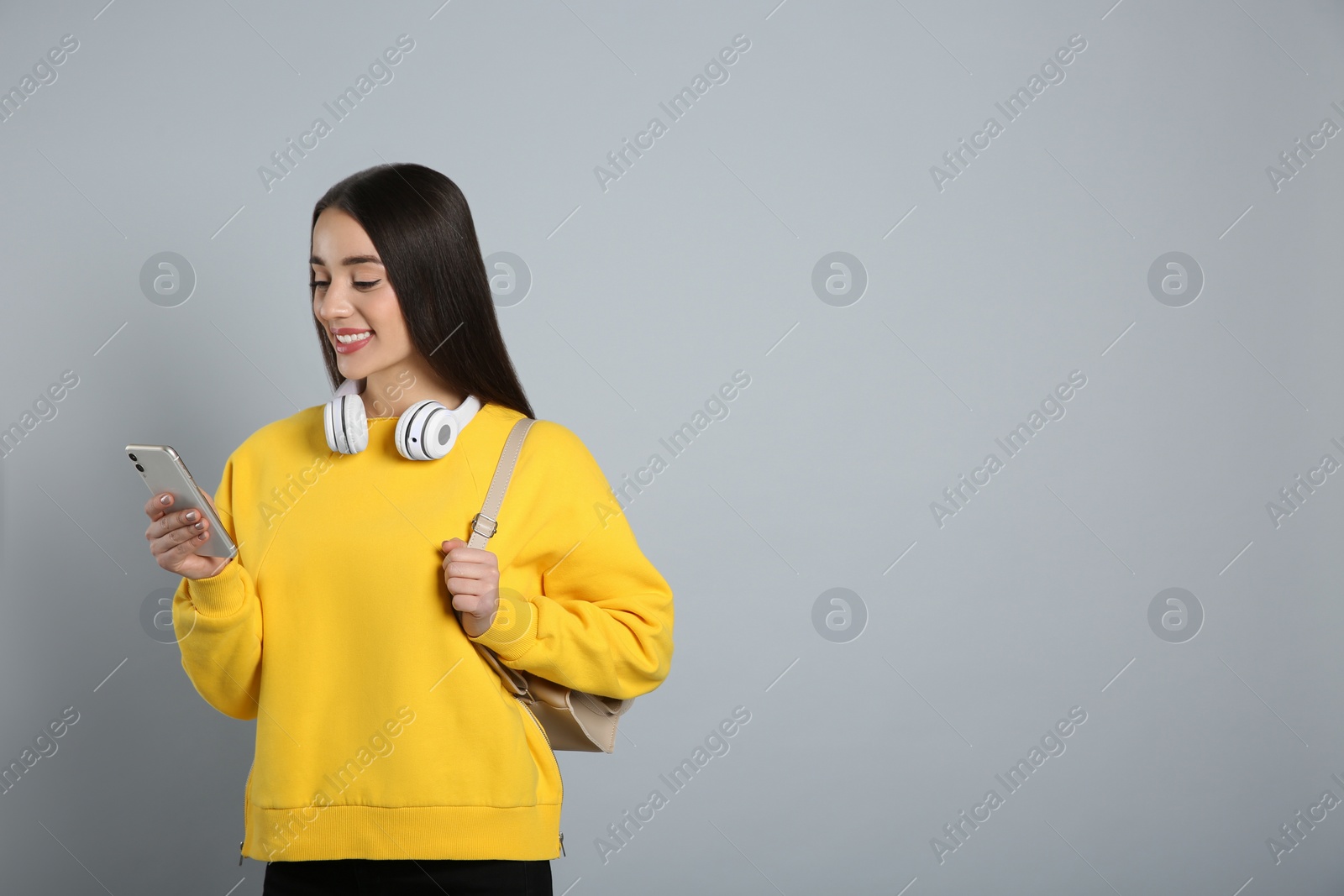 Photo of Beautiful young woman with stylish leather backpack 
 and smartphone on grey background. Space for text