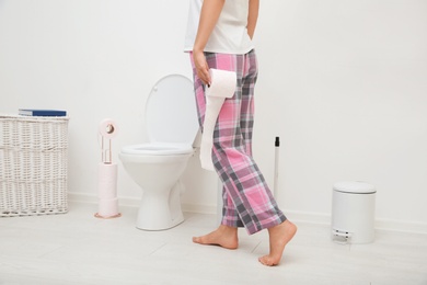 Woman with toilet paper roll standing in bathroom