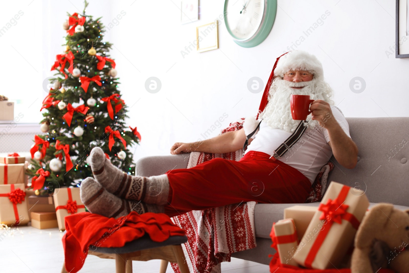 Photo of Authentic Santa Claus resting with cup of tea on sofa indoors