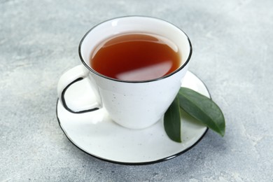 Aromatic tea in cup and green leaves on grey table