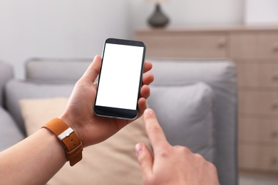 Man holding smartphone with blank screen indoors, closeup of hands. Space for text