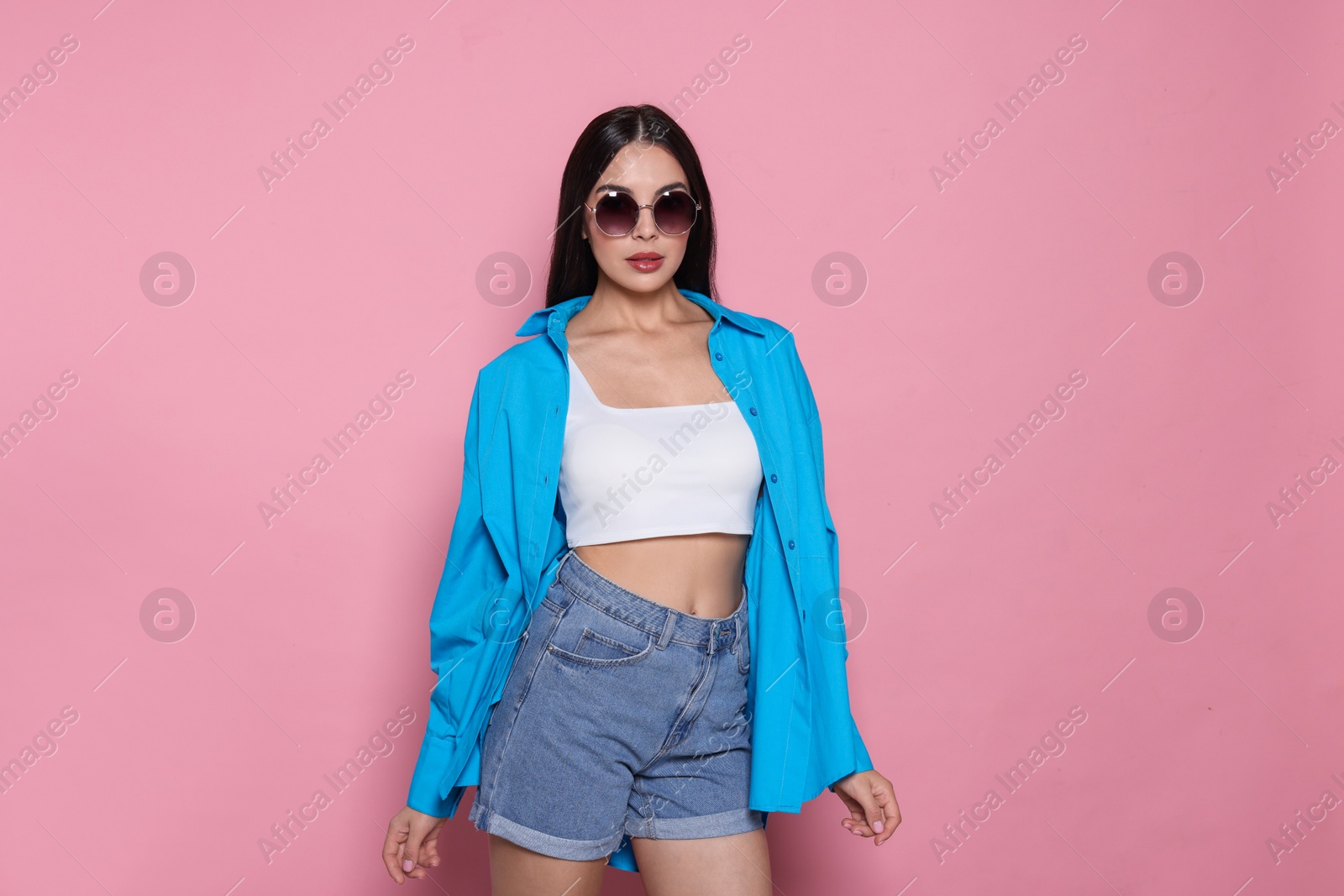 Photo of Attractive serious woman in fashionable sunglasses against pink background. Space for text