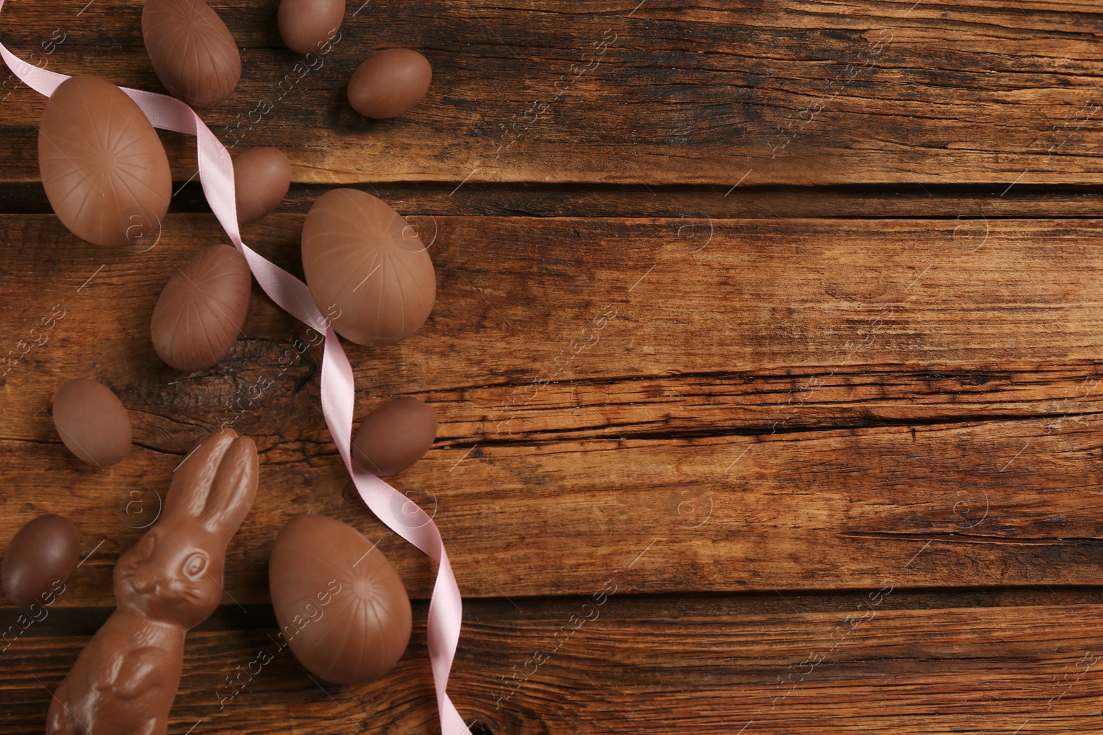 Photo of Sweet chocolate eggs and bunny on wooden table, flat lay. Space for text