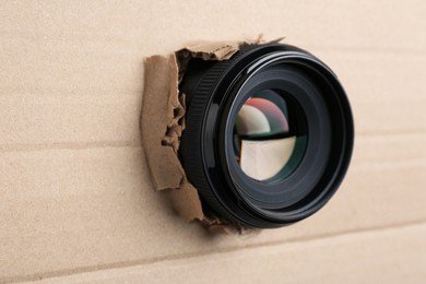 Hidden camera lens through torn in cardboard, closeup