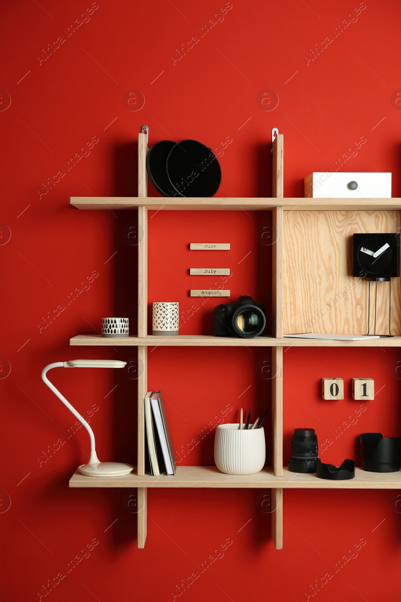 Photo of Stylish wooden shelves with photography equipment and decorative elements on red wall