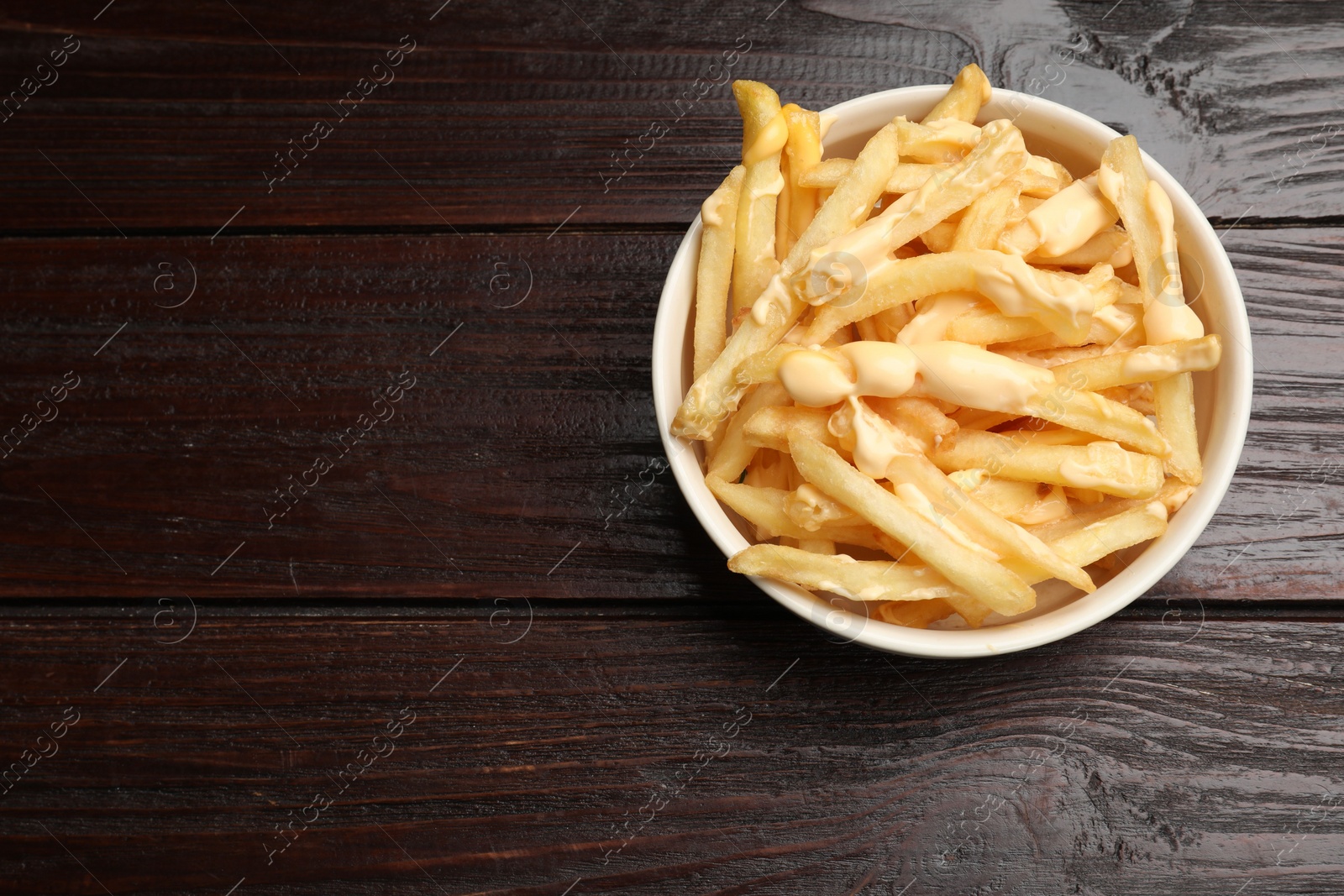 Photo of Delicious french fries with cheese sauce in bowl on wooden table, top view. Space for text