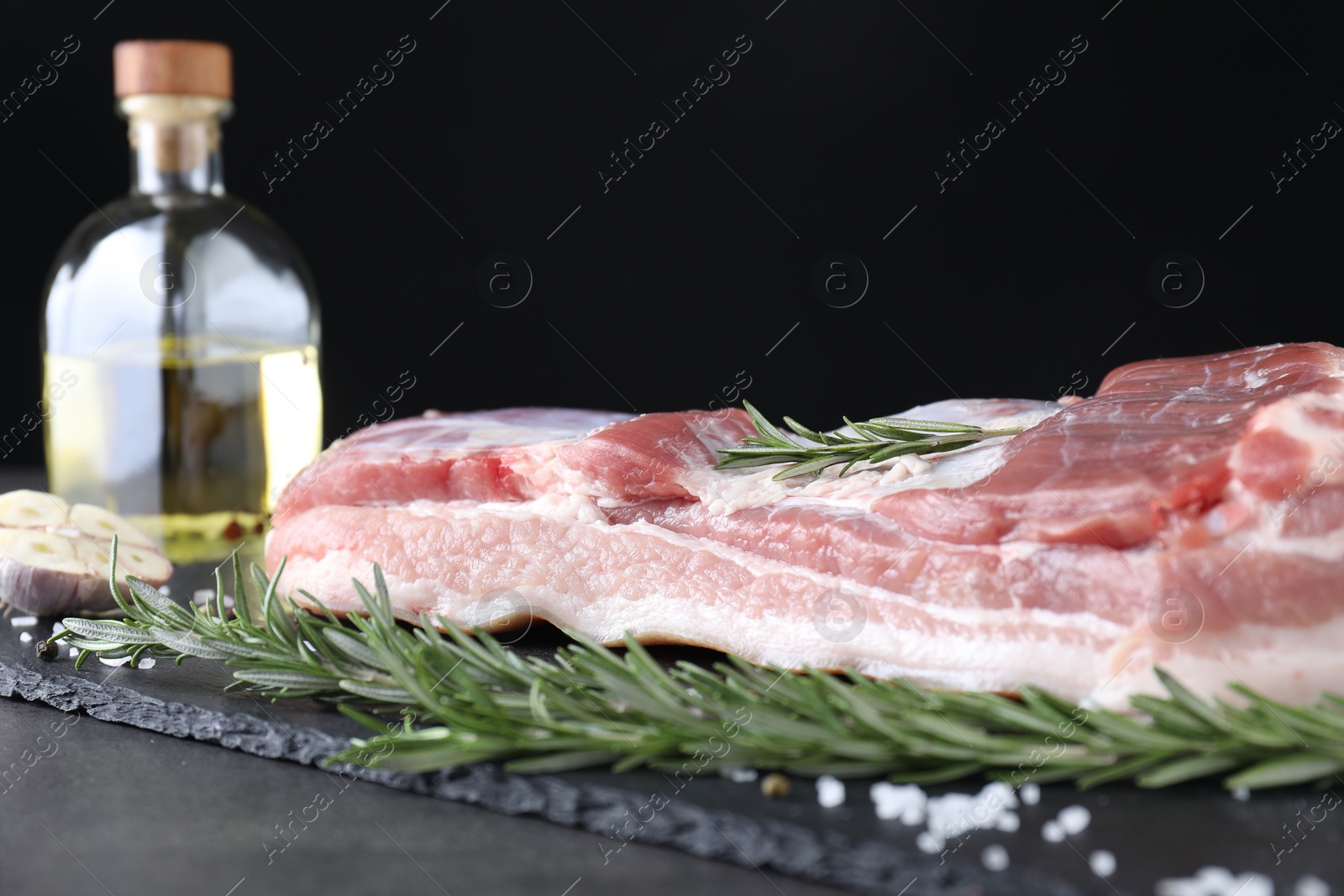 Photo of Piece of raw pork belly, rosemary and salt on grey table, closeup