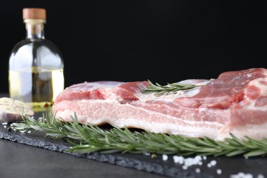 Piece of raw pork belly, rosemary and salt on grey table, closeup