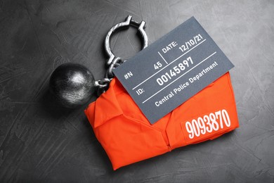 Metal ball with chain, prison uniform and mugshot letter board on grey table, flat lay