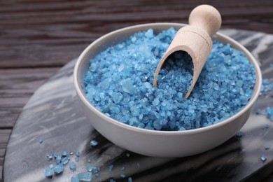 Photo of Bowl and scoop with blue sea salt on dark wooden table, closeup