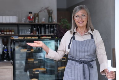 Photo of Happy business owner inviting to come into her cafe, space for text