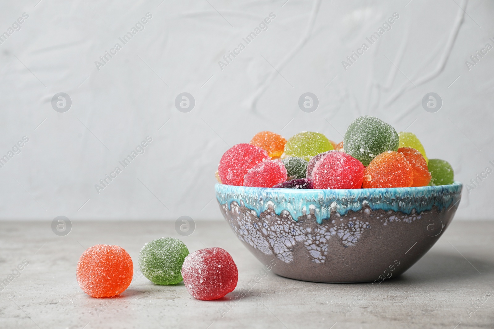 Photo of Bowl with delicious colorful candies on table against gray background. Space for text