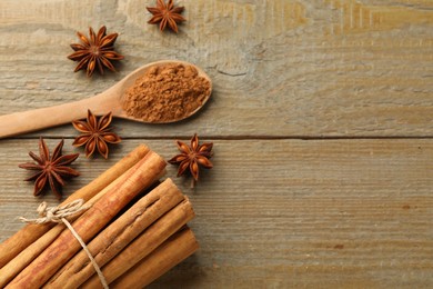 Photo of Spoon with cinnamon powder, sticks and star anise on wooden table, flat lay. Space for text