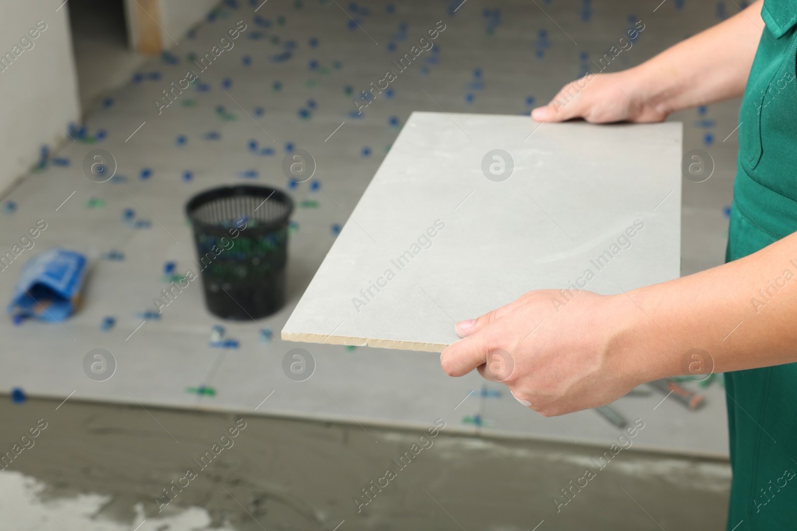 Photo of Worker holding tile near adhesive mix on floor, closeup