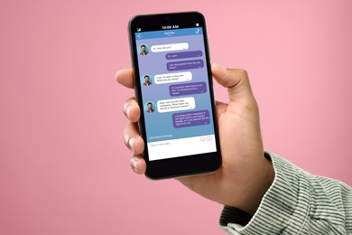Image of Man texting with friend using messaging application on smartphone against pink background, closeup