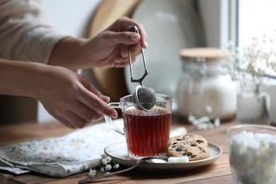 Photo of Young woman using snap infuser for brewing tea at wooden table, closeup