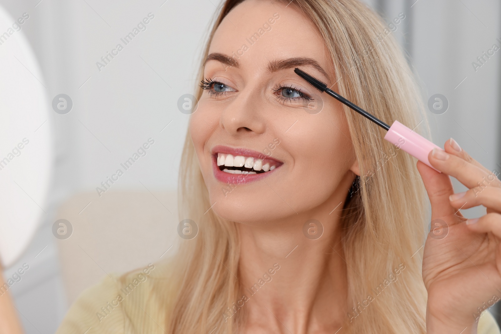 Photo of Beautiful woman applying mascara with brush indoors, closeup