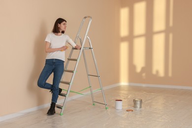 Photo of Young woman with roller near metal stepladder indoors. Room renovation