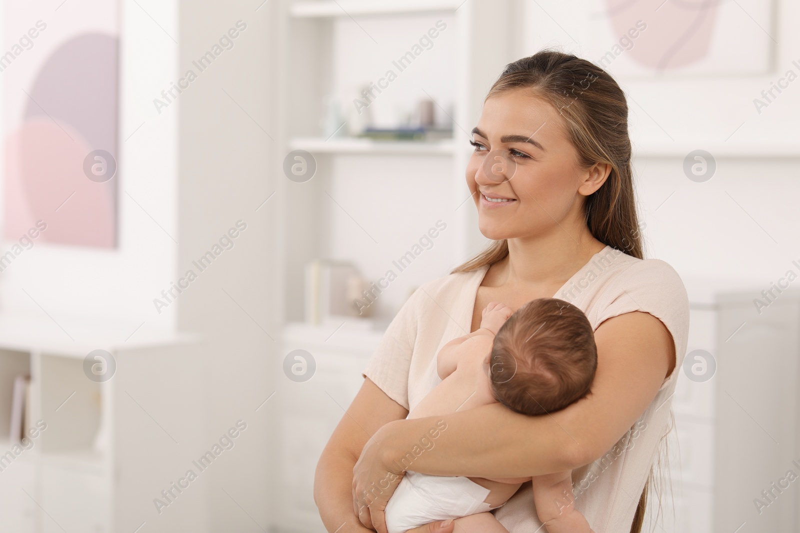 Photo of Mother holding her cute newborn baby in child's room, space for text