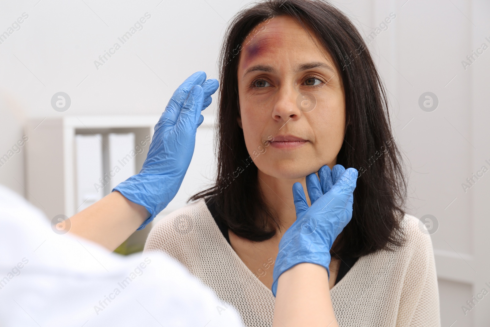 Photo of Doctor examining woman with bruise on forehead in clinic
