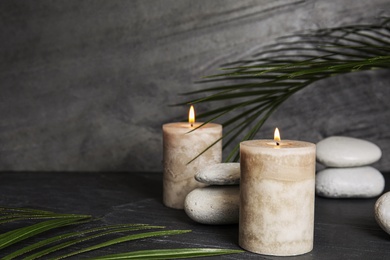 Photo of Burning candles and spa stones on dark table, space for text