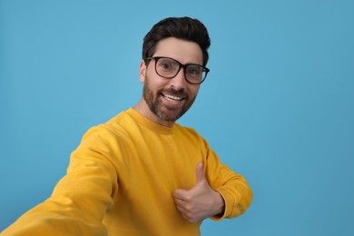 Photo of Smiling man taking selfie and showing thumbs up on light blue background
