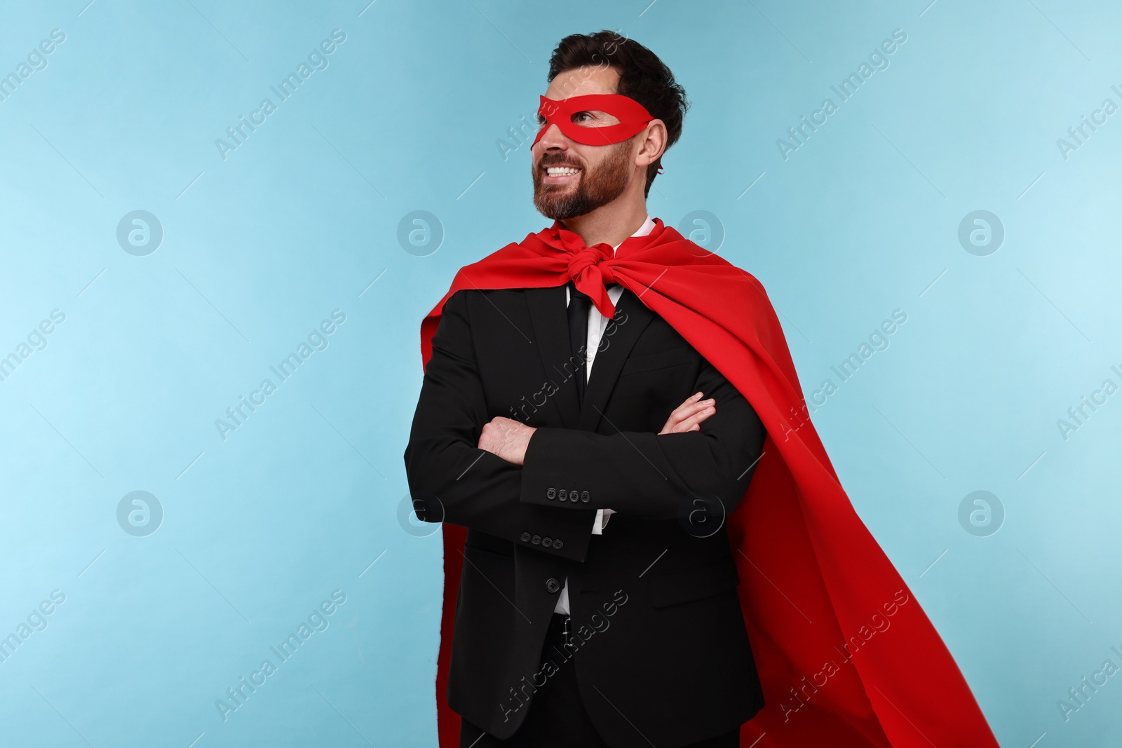 Photo of Businessman wearing red superhero cape and mask on light blue background