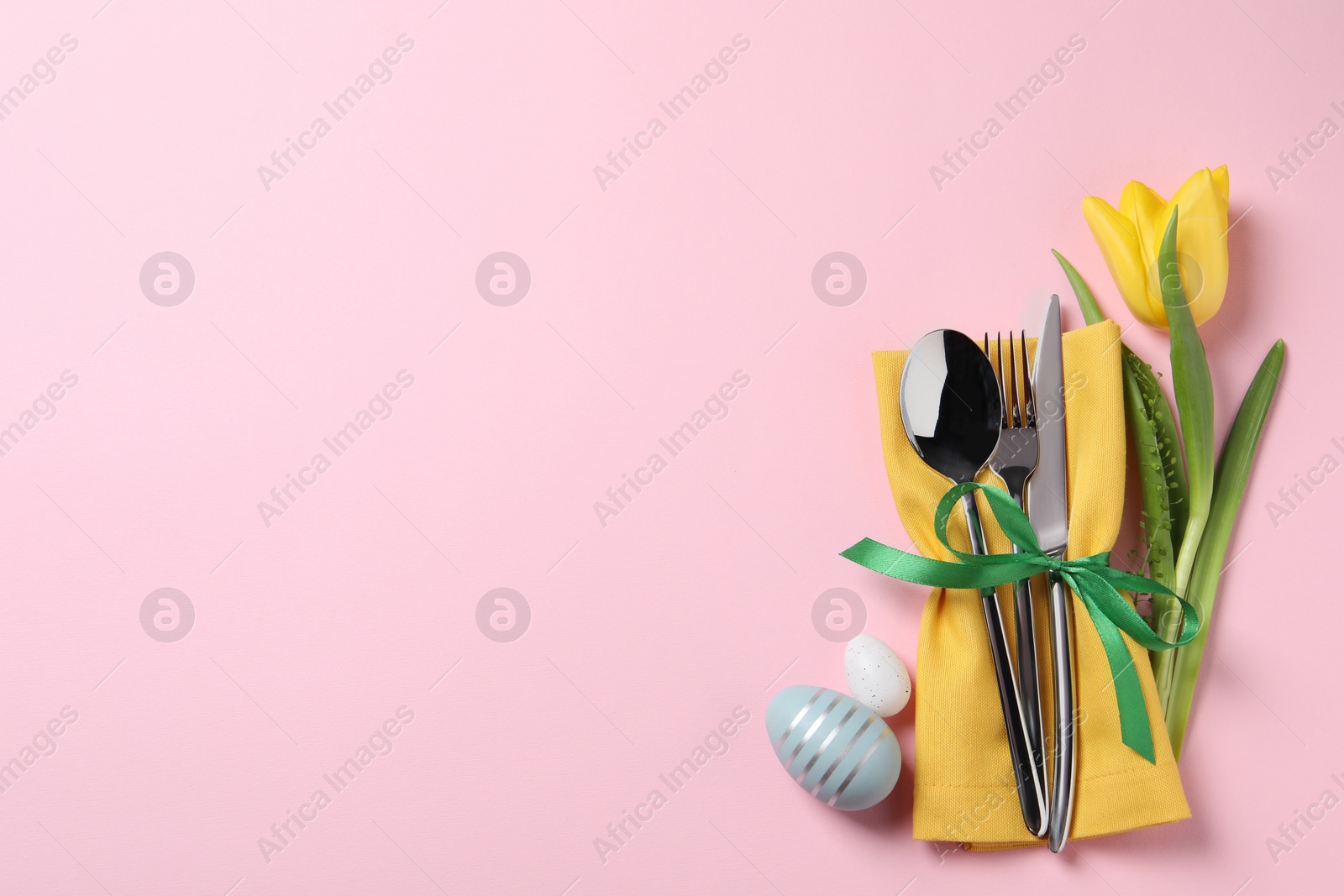 Photo of Cutlery set, Easter eggs and tulip on pale pink background, flat lay with space for text. Festive table setting