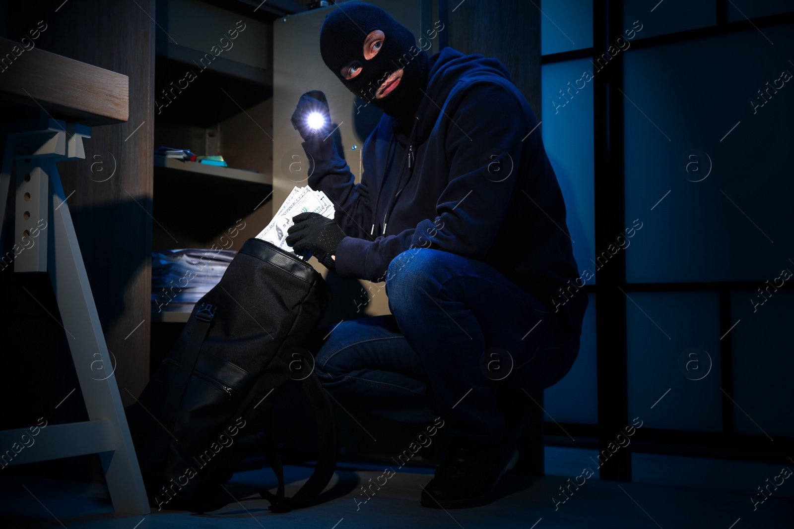 Photo of Thief taking money out of steel safe indoors at night