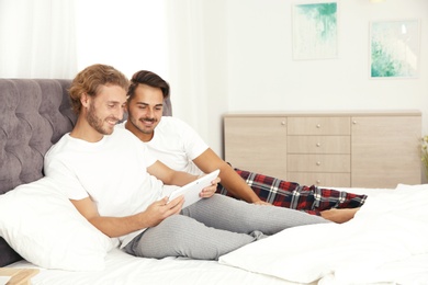 Happy gay couple with tablet computer on bed at home