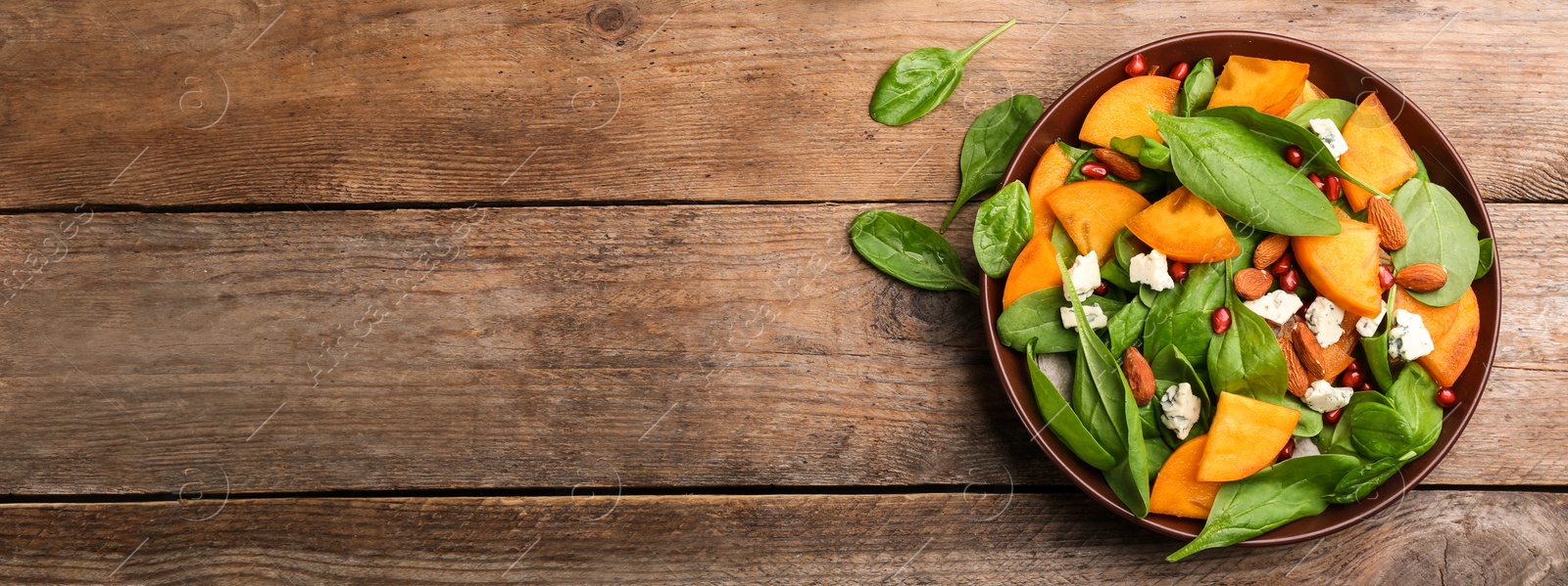 Image of Delicious persimmon salad served on wooden table, top view with space for text. Banner design