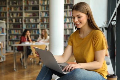 Photo of Young woman working on laptop in library. Space for text