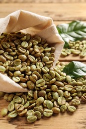 Photo of Sackcloth bag with green coffee beans and leaves on wooden table, closeup