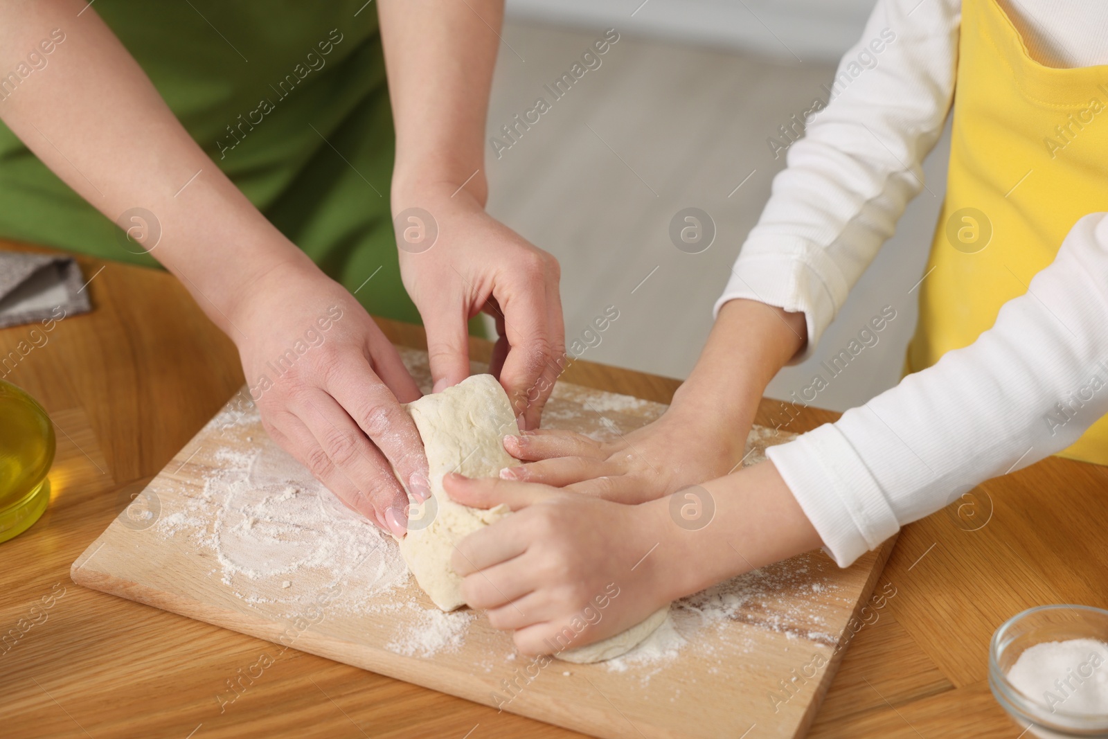 Photo of Making bread. Mother and her daughter kneading dough at wooden table indoors, closeup