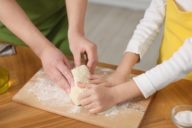 Making bread. Mother and her daughter kneading dough at wooden table indoors, closeup