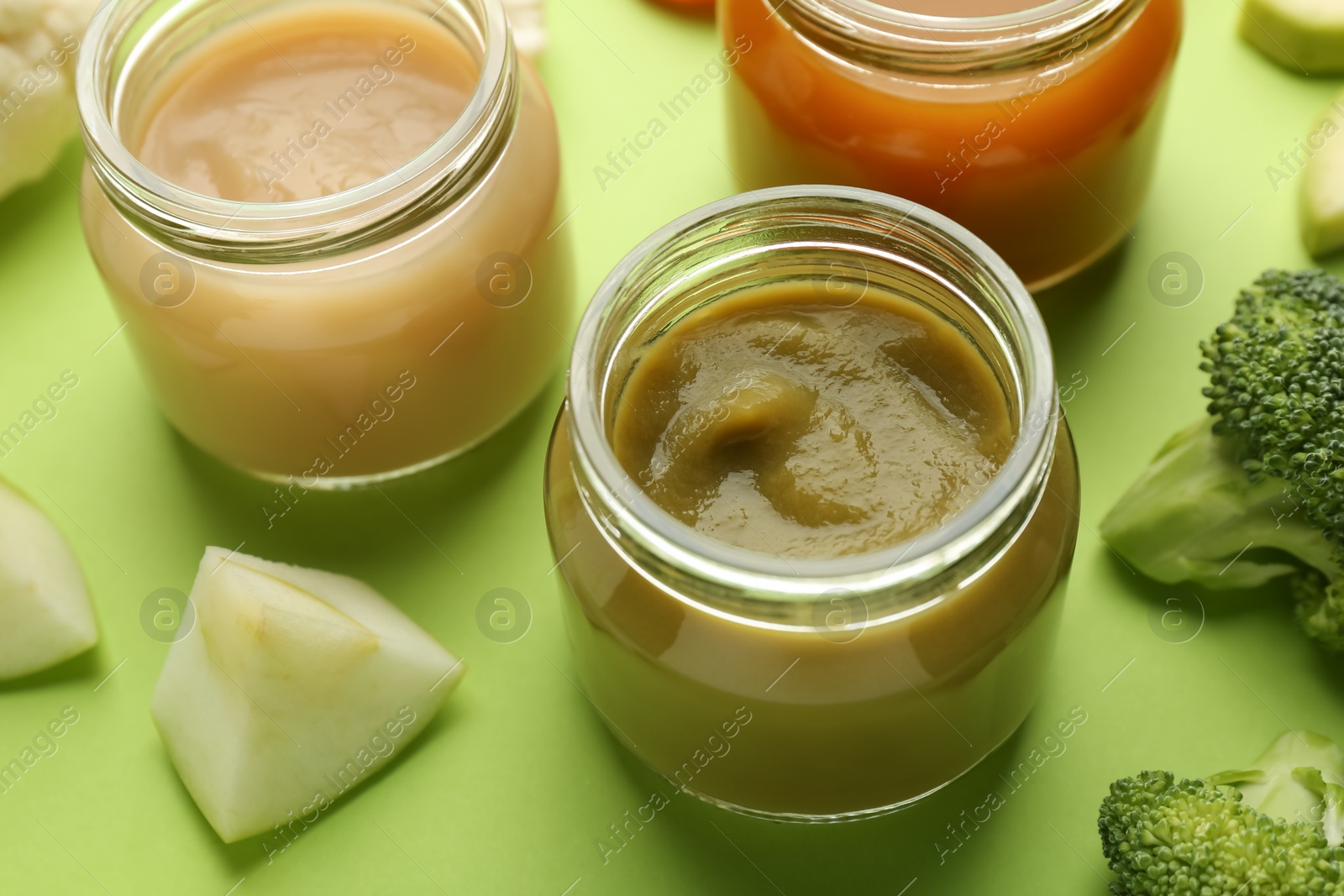 Photo of Jars with healthy baby food, broccoli and apple on light green background, closeup