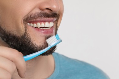 Photo of Man brushing his teeth with plastic toothbrush on white background, closeup. Space for text