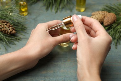 Photo of Woman applying pine essential oil on hand at light blue wooden table, closeup