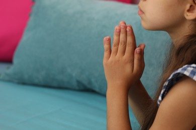 Photo of Cute little girl with hands clasped together praying on bed, closeup. Space for text