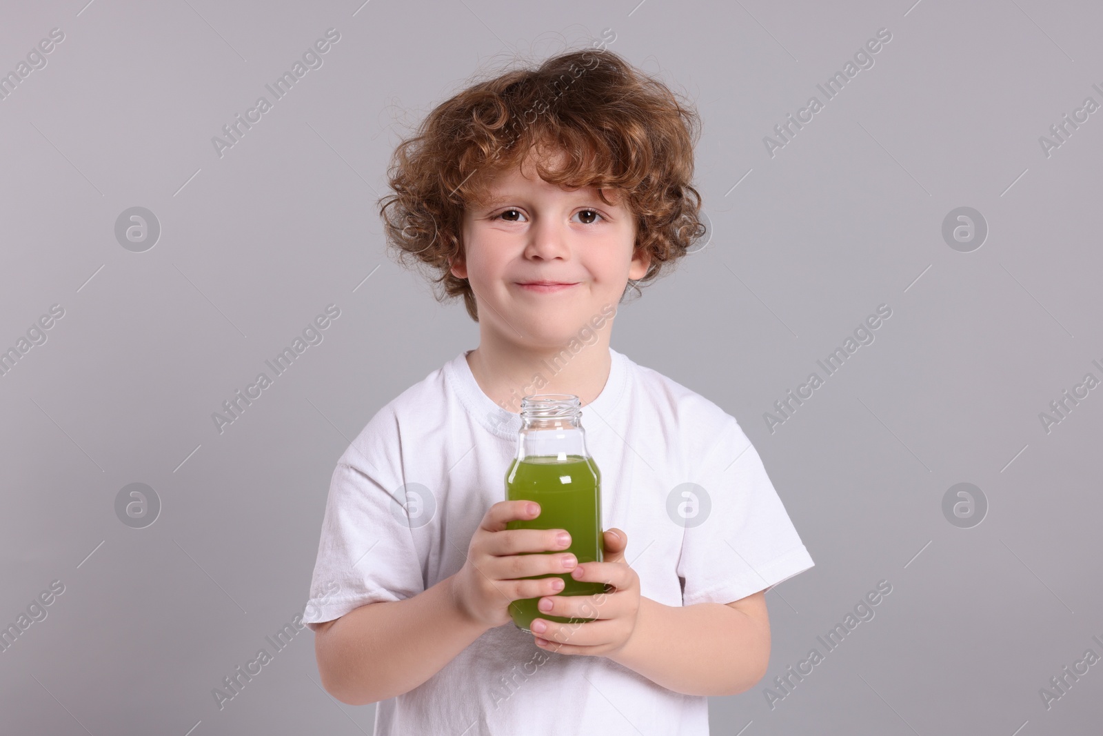 Photo of Cute little boy with glass bottle of fresh juice on light gray background