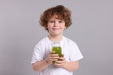 Cute little boy with glass bottle of fresh juice on light gray background