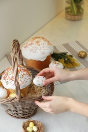 Woman putting dyed eggs in basket with traditional Easter cake at table, closeup