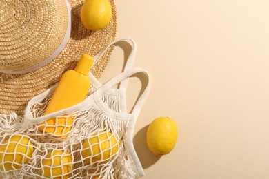 String bag with fresh lemons, sunscreen and straw hat on beige background, flat lay. Space for text